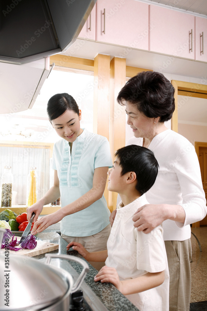 Woman cutting vegetables, another woman and boy watching Woman cutting vegetables, another woman and boy watching