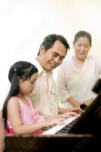 Senior man and girl playing the piano while senior woman looks on