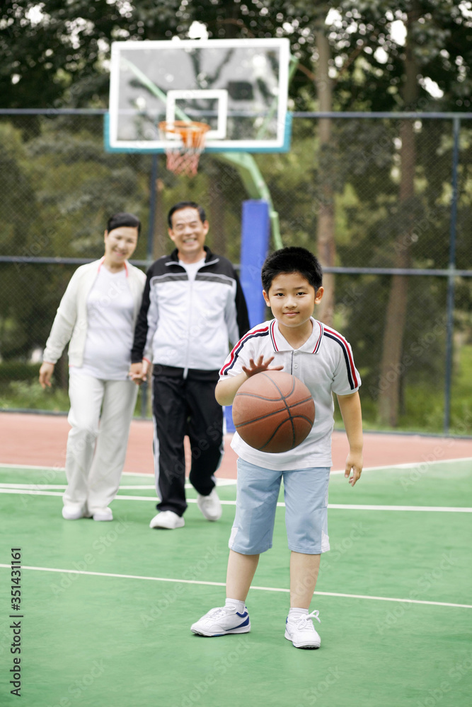 Obraz premium Boy dribbling basketball, senior man and woman watching