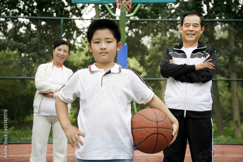 Boy holding basketball, senior man and woman standing behind him