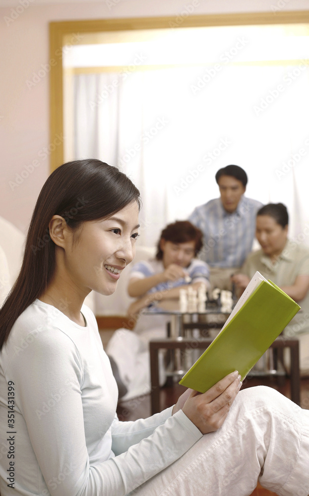 Woman reading book with people playing chess game in the background Woman reading book with people playing chess game in the background
