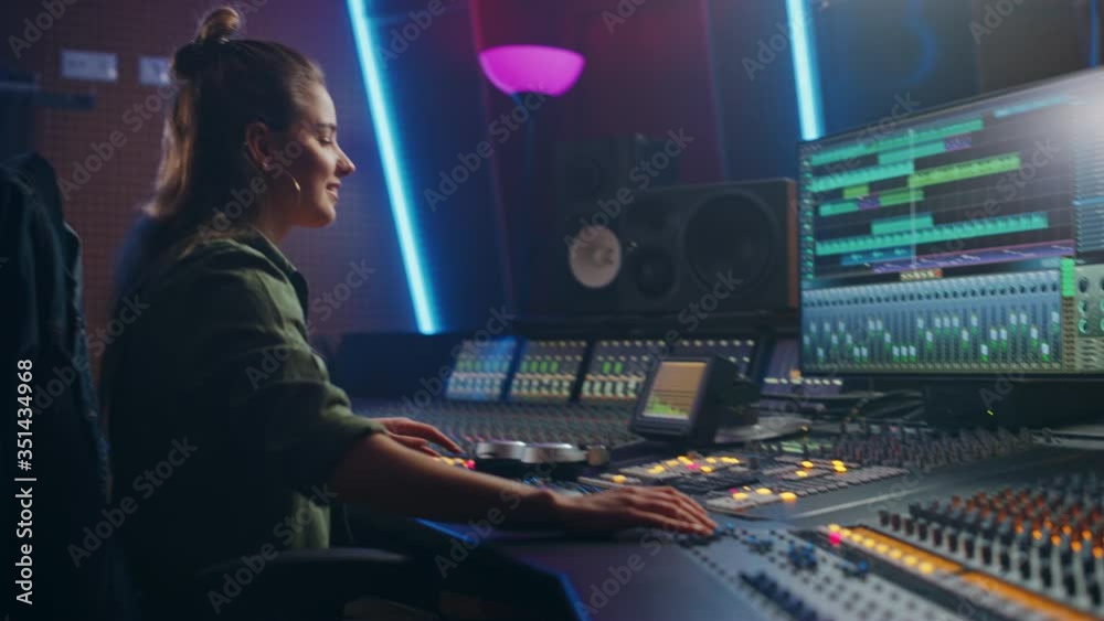 Female Audio Engineer Working in Music Recording Studio, Uses Mixing Board Create Song. Successful Girl Artist Musician Working at Control Desk. Having Fun, Smiling, Dancing. Handheld Arc Shot Female Audio Engineer Working in Music Recording Studio, Uses Mixing Board Create Song. Successful Girl Artist Musician Working at Control Desk. Having Fun, Smiling, Dancing. Handheld Arc Shot
