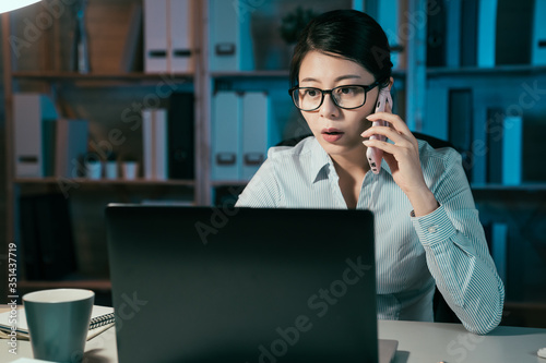 confident businesswoman in glasses overtime work and speak on smart phone. beautiful office lady hardworking on laptop computer in dark night at company and talking on cellphone with coworker.