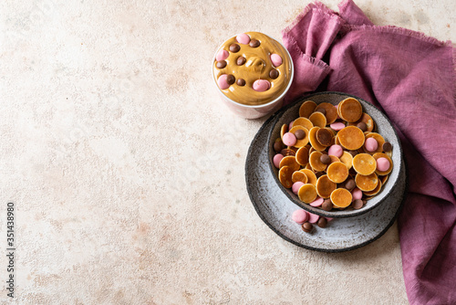 Small pancakes cereal in ceramic bowl on light beige background. Dalgona coffee and tiny pancakes cereal Served with pink and milk chocolate drops