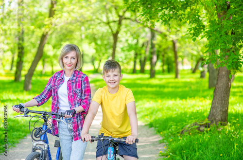 Sporty family, mother and her young son, ride a bike in summer park. Empty space for text