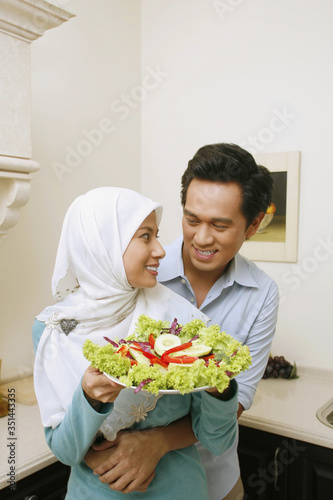 Woman holding salad  man hugging her from behind