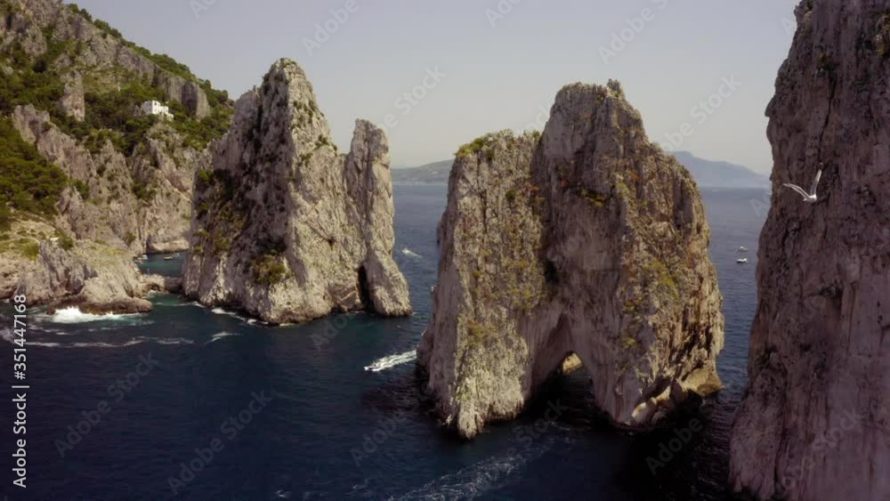 Aerial view of seagull flying over sea near stack rocks on sunny day, sea bird moving over water against rocky mountain - Capri, Italy Aerial view of seagull flying over sea near stack rocks on sunny day, sea bird moving over water against rocky mountain - Capri, Italy