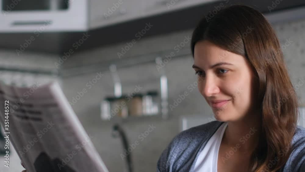 Newspaper News. World pandemic. Source of news. Read newspaper. Attractive female reads a fresh news newspaper while sitting at home in the kitchen. Close-up Newspaper News. World pandemic. Source of news. Read newspaper. Attractive female reads a fresh news newspaper while sitting at home in the kitchen. Close-up