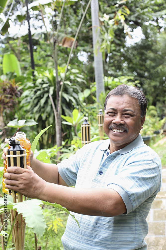 Senior man pouring oil into bamboo torch Senior man pouring oil into bamboo torch