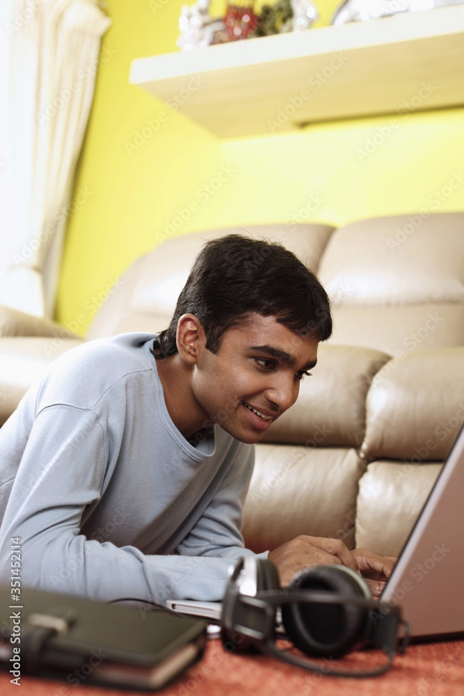 Young man lying forward on the floor, using laptop