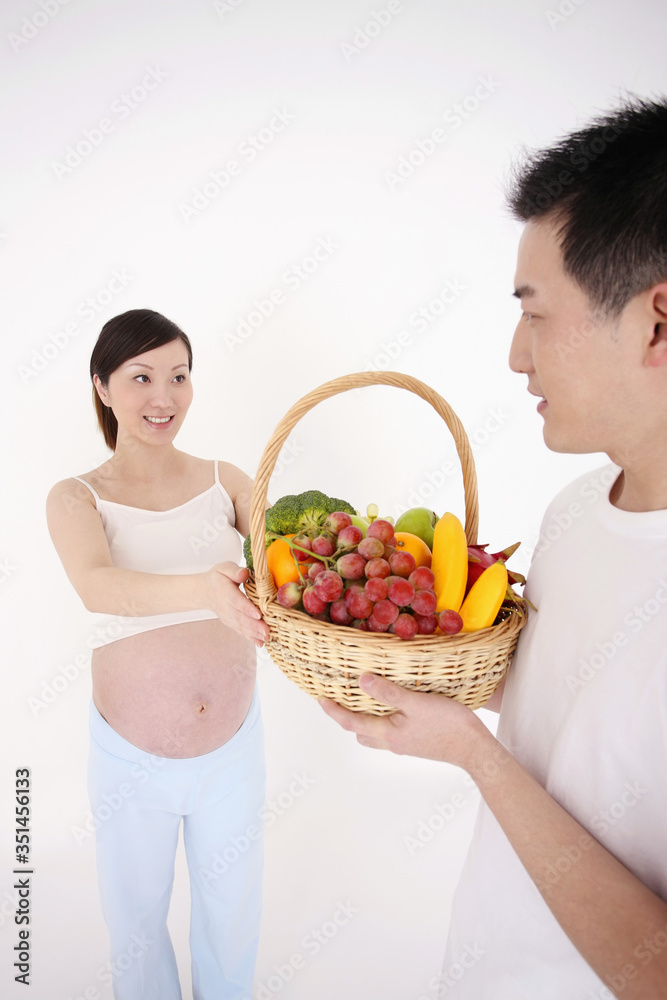 Man giving a basket of fruits and vegetables to pregnant woman Man giving a basket of fruits and vegetables to pregnant woman