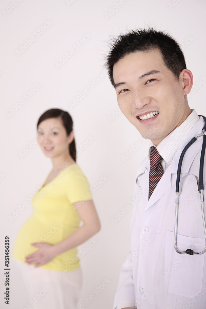 Doctor smiling while pregnant woman is in the background Doctor smiling while pregnant woman is in the background