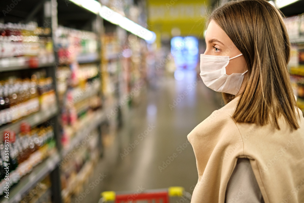 Close-up portrait of young woman wearing protective mask and buying food in grocery store during coronavirus pandemic. Covid-19. Copy space