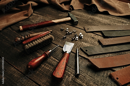 Leather samples and set crafting DIY tools on wooden table background texture. Leather craftmans work desk. Copy space, maintenance concept. Belt production. photo