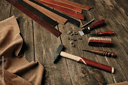 Flat lay composition with leather samples and set crafting DIY tools on wooden table background texture. Leather craftmans work desk. Copy space, maintenance concept. Belt goods production. Top view. photo