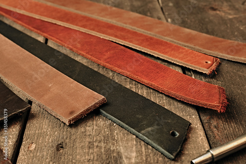 Brown black and netural leather pieces of leather for men's belt on a wooden background, top view. Leather craftmans work desk. Maintenance concept. Belt goods production. photo