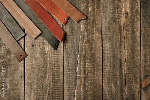 Brown black and netural leather pieces of leather for men's belt on a wooden background, top view. Leather craftmans work desk. Copy space, maintenance concept. Belt goods production. photo