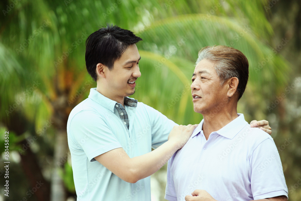 Man giving his father a pat on the shoulder while talking Man giving his father a pat on the shoulder while talking