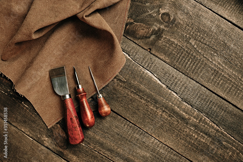 Flat lay composition with leather samples and set crafting DIY tools on wooden table background texture. Leather craftmans work desk. Copy space, maintenance concept. Belt goods production. Top view. photo