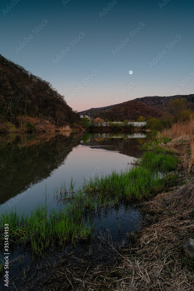 Fototapeta premium A lake in which the moon is reflected among the hills at dusk