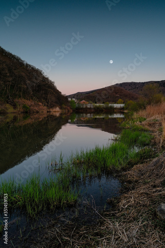 A lake in which the moon is reflected among the hills at dusk