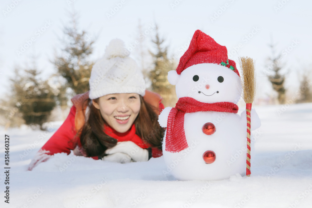 Woman in warm clothing lying on snow and looking at snowman Woman in warm clothing lying on snow and looking at snowman