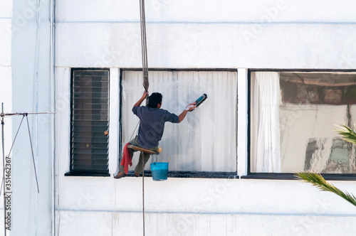Trabajador limpia ventana exterior en edificio de Ciudad de México con pocas medidas de seguridad photo