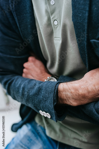 selective focus, no face, man in a blue jacket with buttons on the sleeves and a gray Polo crossed tanned hands with dark hair and a watch