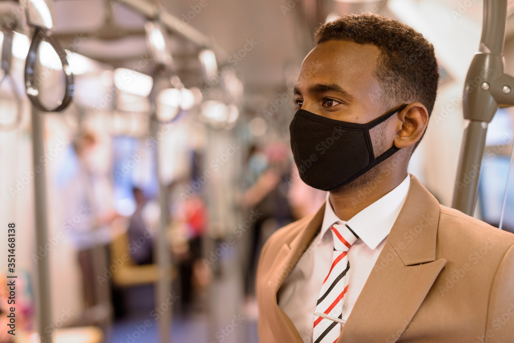 Face of young African businessman wearing mask and standing with distance inside the train Face of young African businessman wearing mask and standing with distance inside the train