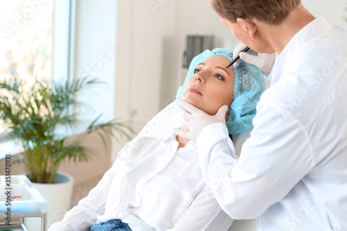 Plastic surgeon applying marks on woman s face in clinic