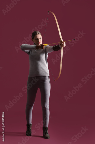 Beautiful woman with crossbow on color background