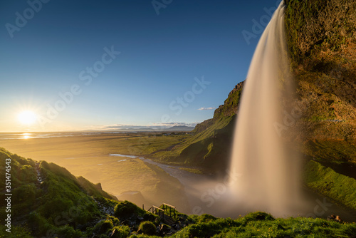 Panorama scene Sundown and powerful of white streaming at Seljalandsfoss waterfall with green bush in foreground, Summer,Iceland