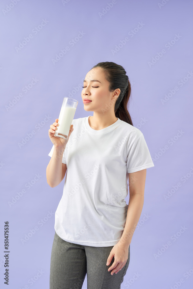 Portrait of a satisfied young asian woman drinking milk from the glass isolated over purple background Portrait of a satisfied young asian woman drinking milk from the glass isolated over purple background