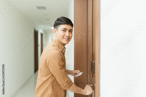 Young man holding a keycard in front of the electronic sensor of a room door
