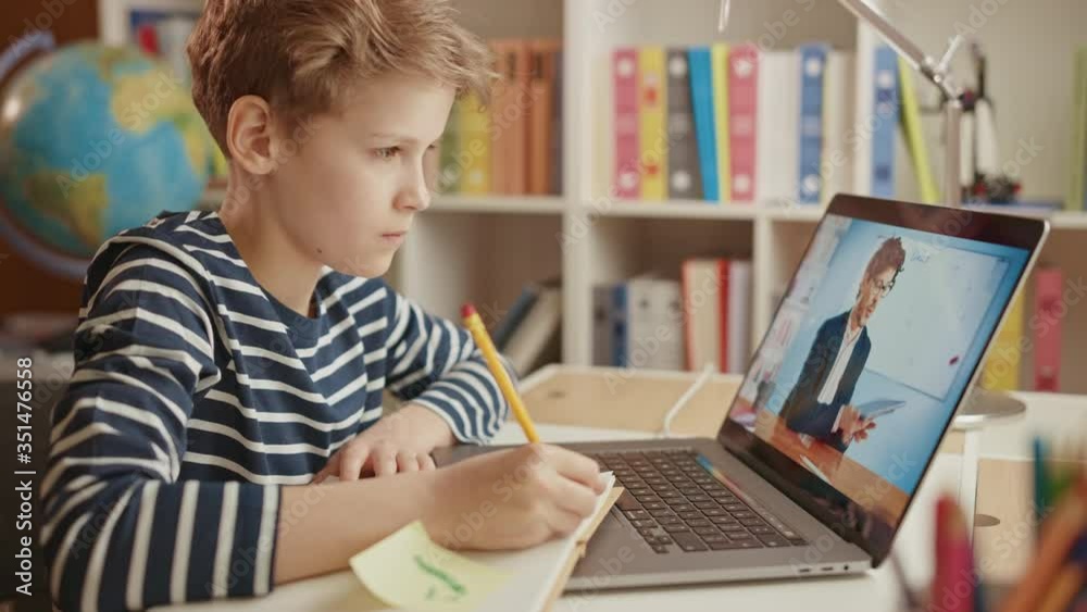 Smart Little Boy Uses Laptop for Video Call with His Teacher. Screen Shows Online Lecture with Teacher Explaining Subject from a Classroom, Boy writes Down Information. E-Education Distance Learning Smart Little Boy Uses Laptop for Video Call with His Teacher. Screen Shows Online Lecture with Teacher Explaining Subject from a Classroom, Boy writes Down Information. E-Education Distance Learning