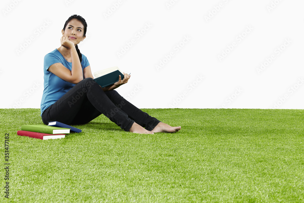 Young woman sitting on grass reading a book Young woman sitting on grass reading a book