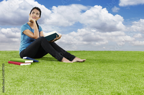 Young woman sitting on grass reading a book