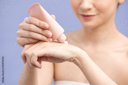 Happy woman hydrating hands skin with moisturizer cream on violet background