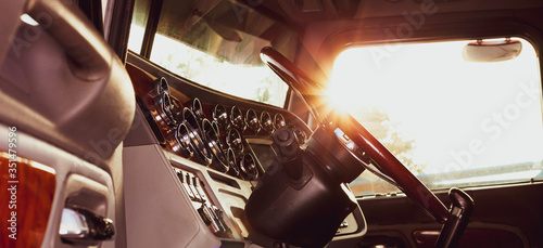 Classic american commercial semi truck with stylish chrome gauges panel and custom luxury wooden steering wheel. Luxurious and comfortable cabin of 18 wheeler truck at evening, back lit, warm filter.