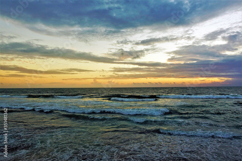 Magical sunset over the Indian Ocean. The waves slowly roll towards the shore, adorned with foam. The clouds are painted with the sun, like watercolors in pink, orange, gold, blue, turquoise. Amazing 