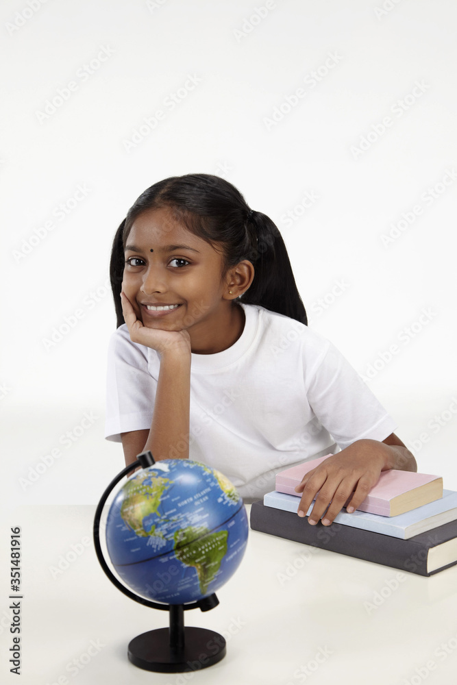 Girl smiling with hand resting on books and a globe on the table Girl smiling with hand resting on books and a globe on the table