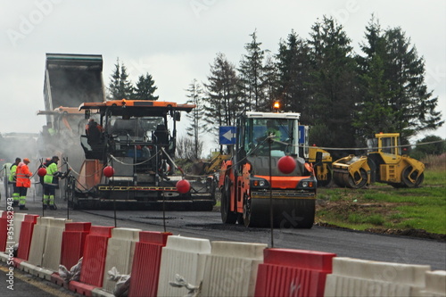 Highway road repair, asphalt compactor skating rink on summer day on green trees background, motorway building mechanization