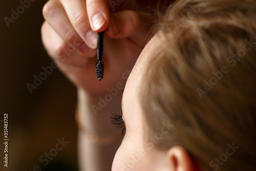 Girl applying mascara on her eye lashes close up