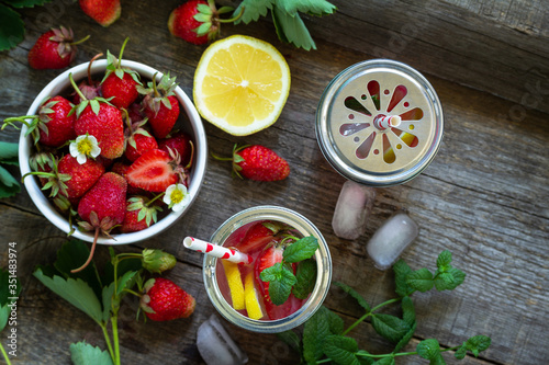 Refreshing Summer drink. Lemonade with fresh strawberries, ice and lemons on a rustic wooden table. Top view flat lay background. Copy space.