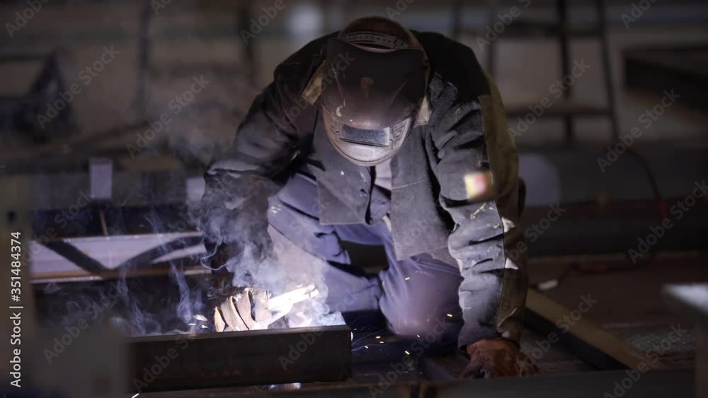 Blacksmith welder in protective mask works with metal steel and iron using welding machine, bright sparks and flashes. Welder uses mask to protect eyes from spark. Professional industry welder working Blacksmith welder in protective mask works with metal steel and iron using welding machine, bright sparks and flashes. Welder uses mask to protect eyes from spark. Professional industry welder working