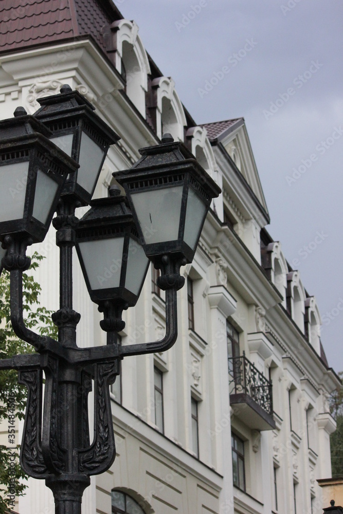 cast iron street lamp consisting of four lamps against the background of the building and the overcast sky