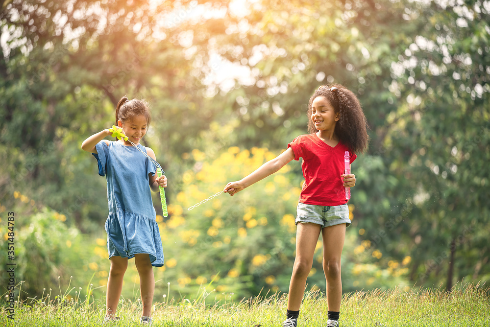Fototapeta premium Cute african american and Asian little girl playing outdoor. Friends happy playing with bubbles together.