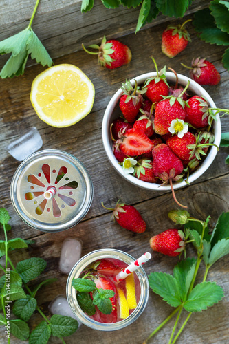 Refreshing Summer drink. Lemonade with fresh strawberries, ice and lemons on a rustic wooden table. Top view flat lay background.