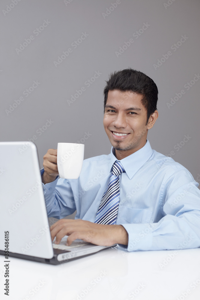 Young businessman enjoying a cup of coffee while working on laptop Young businessman enjoying a cup of coffee while working on laptop