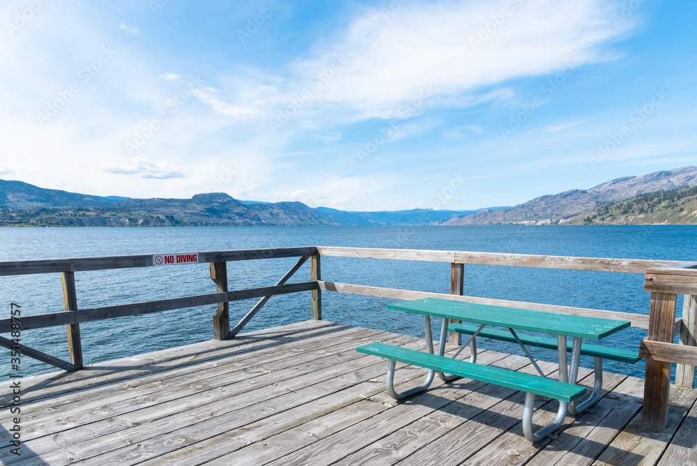 Picnic table on Naramata Wharf with scenic view of Okanagan Lake, mountains, and blue sky Picnic table on Naramata Wharf with scenic view of Okanagan Lake, mountains, and blue sky